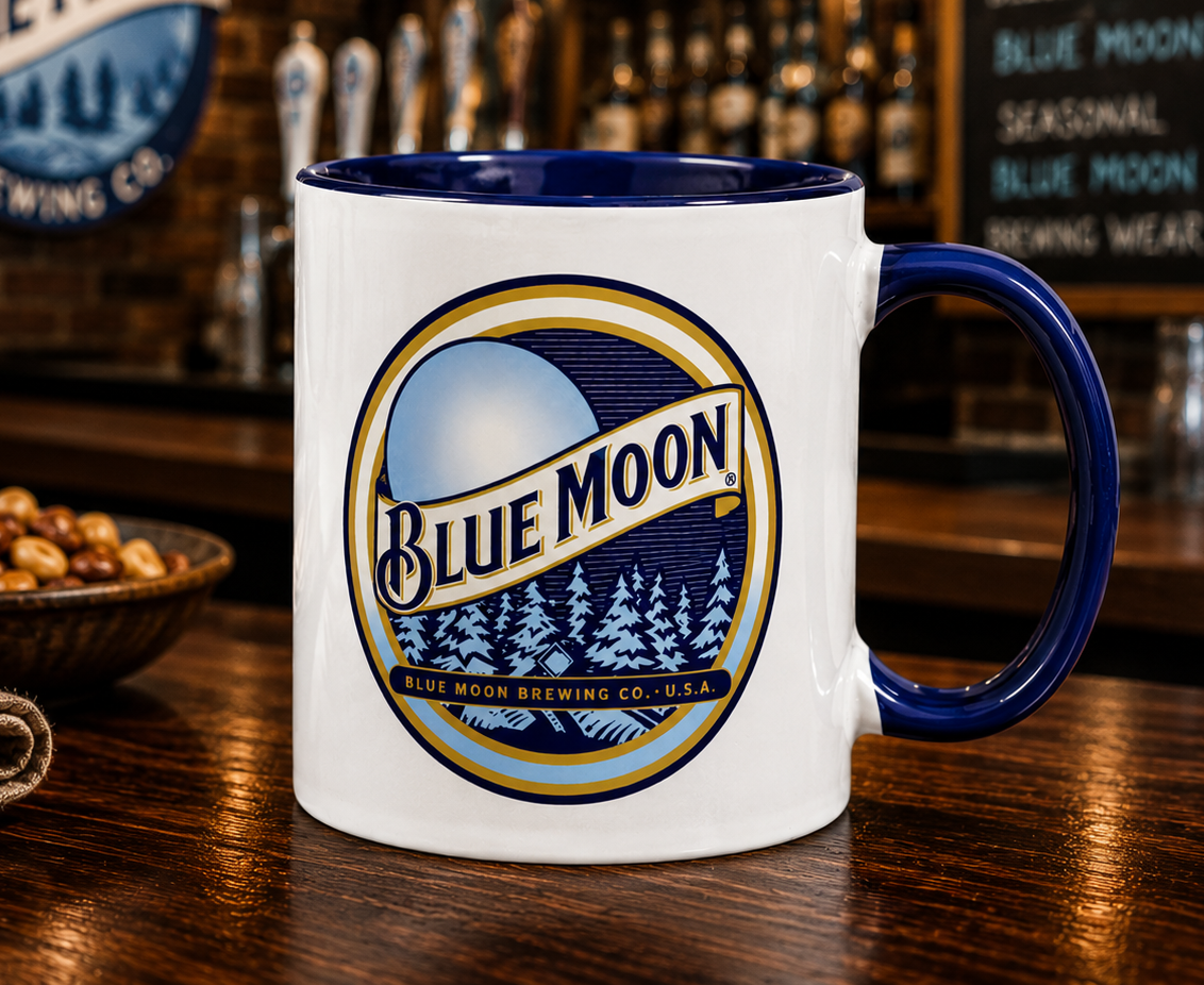 Blue Moon Brewing Company logo coffee mug featuring the iconic moonlit forest design on a white ceramic mug with blue handle, perfect for beer enthusiasts and collectors.